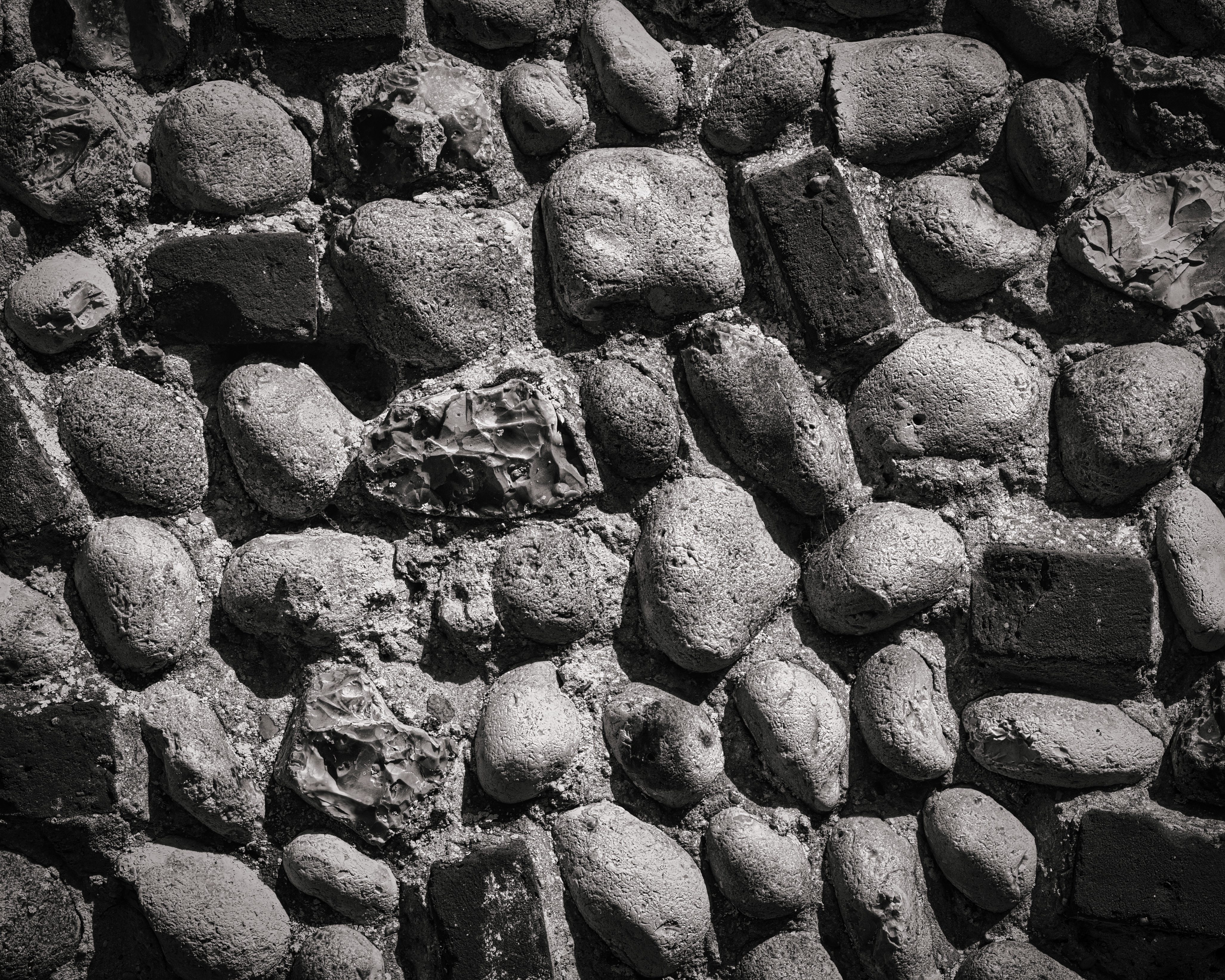This striking black and white photograph captures the raw beauty of a textured stone wall, evoking a timeless elegance of nature. The interplay of light and shadow creates a dramatic, almost ethereal mood, highlighting the unique shapes and textures of each stone. The composition is both focal point, drawing the eye across the entire surface. Its aesthetic appeal lies in its versatility, making it a perfect wall decor for a modern minimalist, the executive office seeking a perfect balance of sophistication and simplicity, or the contemporary gallery wall enthusiast. Display it as a standalone piece or as part of a larger art collection to enhance any room's ambiance.