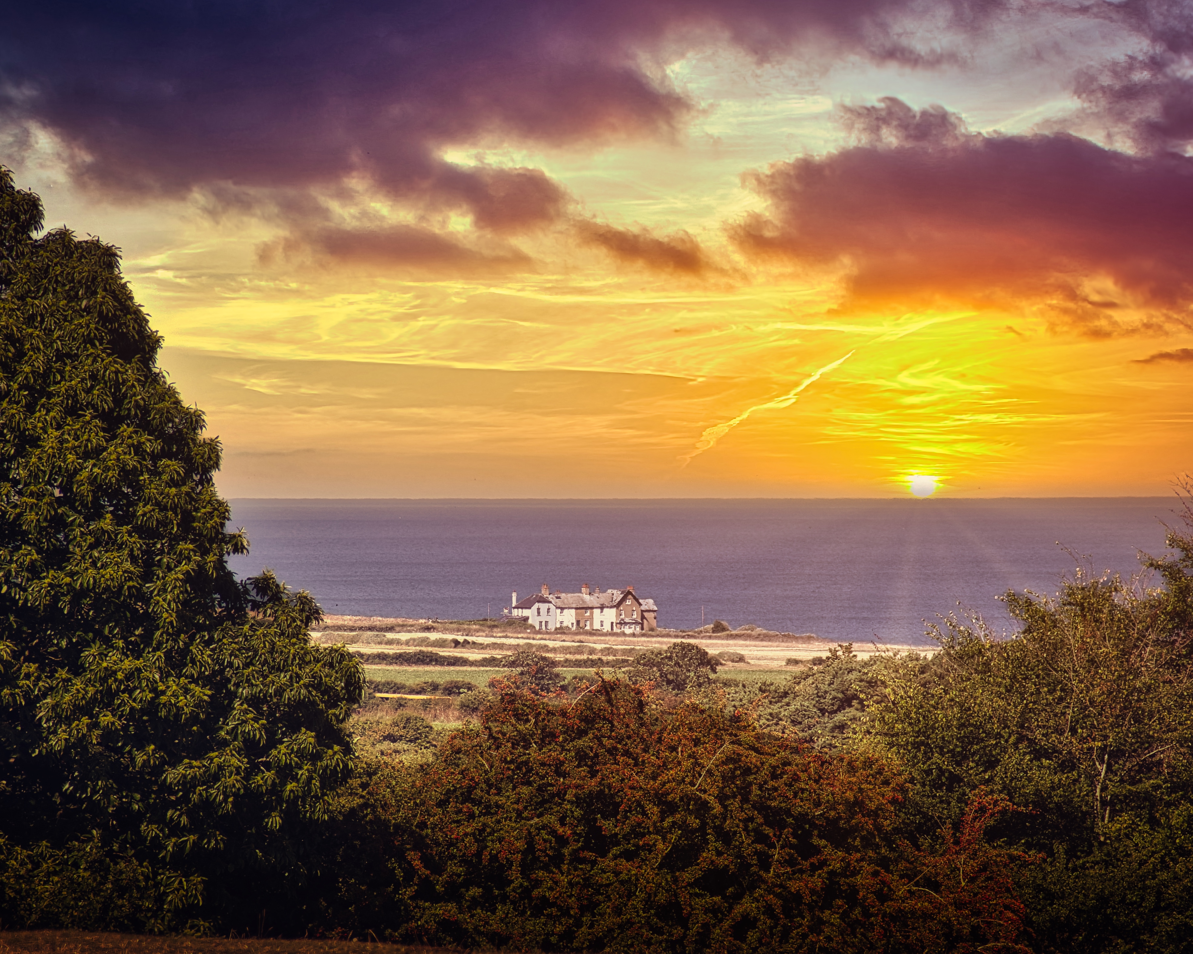 This breathtaking photograph captures the tranquil beauty of a coastal sunset, where the golden hues of the sun blend seamlessly with the deep blue of the ocean. The composition is balanced, with the house nestled in center, framed by lush greenery in foreground and the vast expanse of the sea in background. The warm lighting evokes a feeling of peace and relaxation, making it perfect for a living room as a focal piece or the executive office as a calming backdrop. The aesthetic appeal lies in its ability to transport viewers to a serene beauty of nature, making it a ideal choice for those seeking to infuse their space with a essence of tranquility and natural splendor.