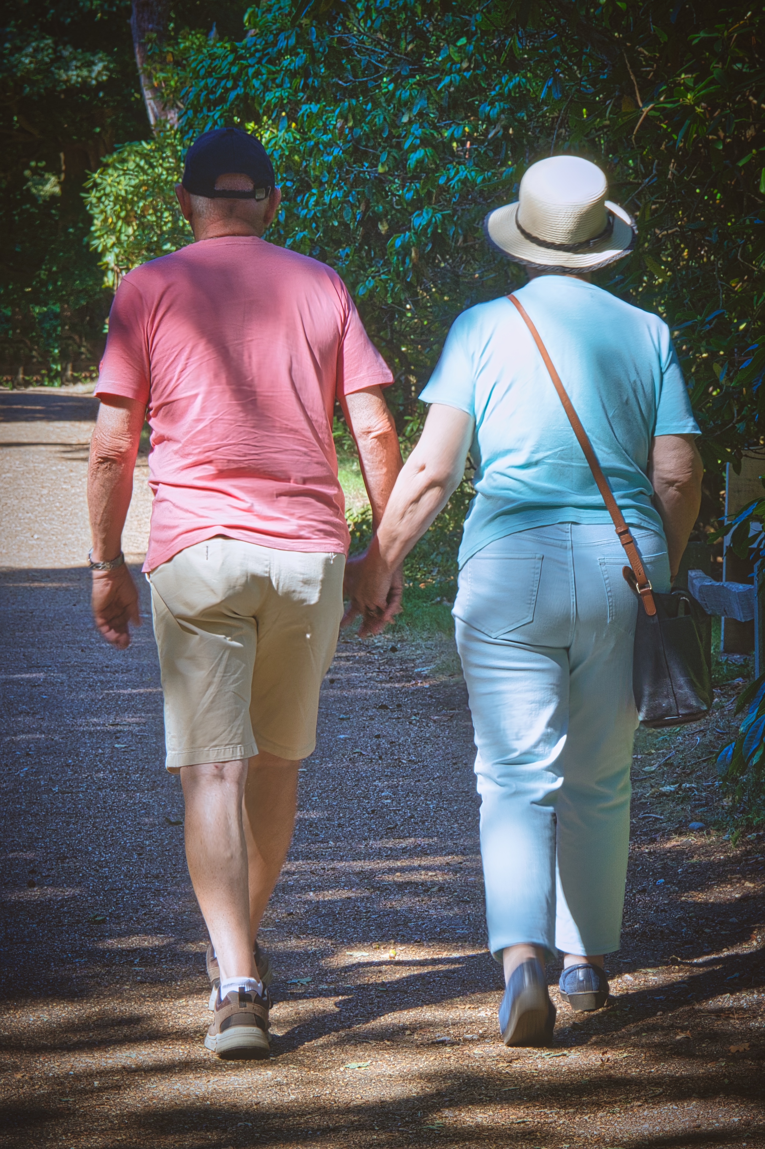 This photograph captures a tender moment between two individuals, their hands intertwined as they stroll through a sun-dappled forest path. The soft, natural lighting enhances the serene and intimate mood, while the vibrant colors of their clothing and the lush greenery create a perfect balance of warmth and tranquility. The composition, with the couple positioned in the center, draws the viewer's eye into the scene, inviting them to feel the quiet companionship and shared journey. This image is ideal for wall decor in a living room, serving as a focal piece that evokes feelings of love and harmony, or in executive office, where it can inspire a spirit of collaboration and partnership.