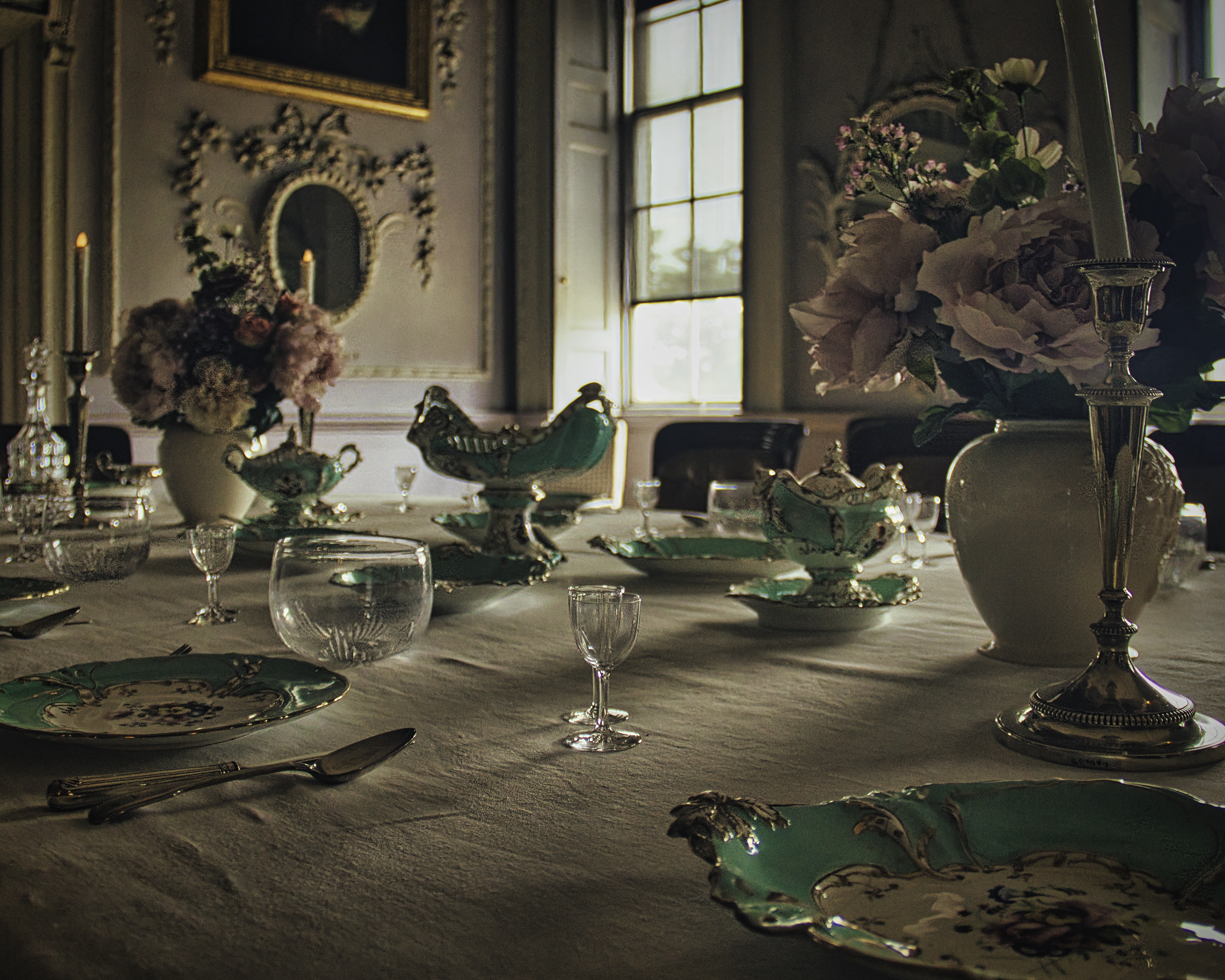 This photograph captures the essence of refined elegance with its meticulously arranged dining table, adorned with antique green and white porcelain, crystal glassware, and lush floral arrangements. The soft, natural light streaming through the window enhances the rich textures and colors, creating a perfect ambiance for a sophisticated dining experience. The composition, with its balanced arrangement of objects and the play of light and shadow, evokes a feeling of timeless luxury. This image would be a perfect focal point for a living room, adding a touch of classic charm to an executive office, or serve as a centerpiece for a modern gallery wall, showcasing the beauty of fine art and decor.
