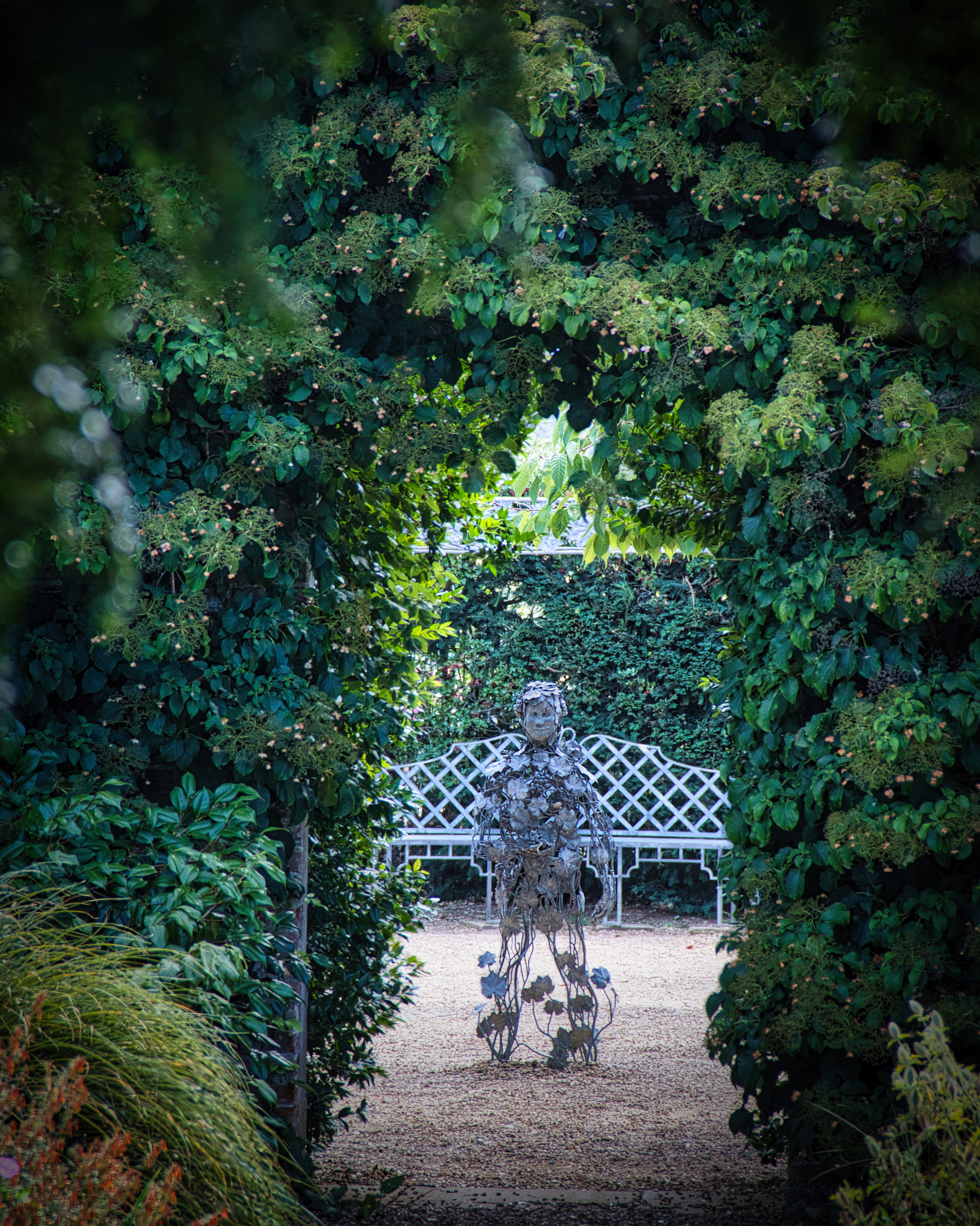 This enchanting fine-art print captures the serene beauty of a garden gate, framed by lush greenery and bathed in soft, natural light. The composition invites viewers into a tranquil world beyond the gate, where a whimsical metal sculpture adds a perfect touch of artistic intrigue. The image's rich, earthy tones and delicate interplay of light and shadow make it a perfect focal piece for any living room or executive office, evoking a sense of calm and inspiration.