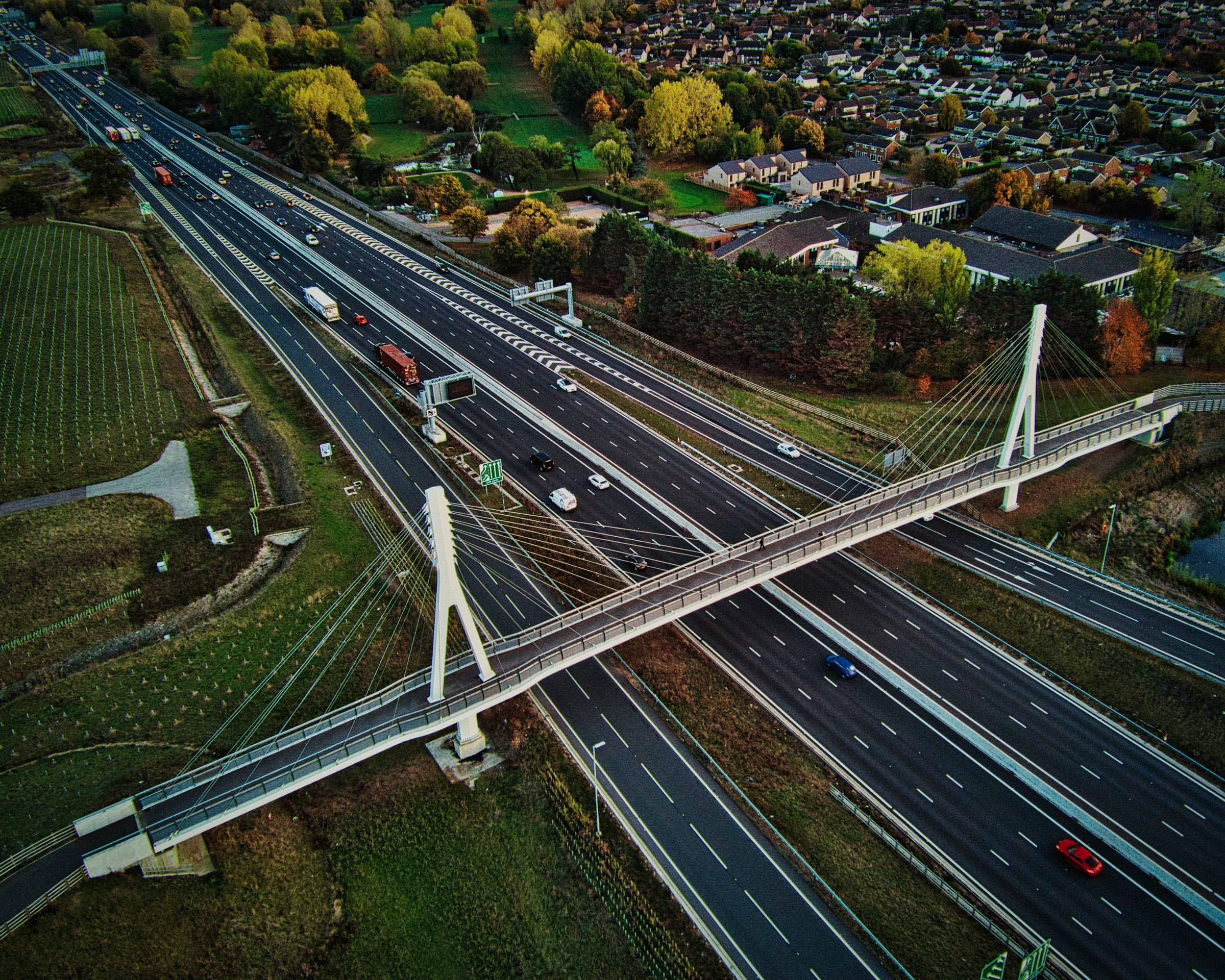 This breathtaking aerial photograph captures the dynamic interplay of urban infrastructure and natural beauty. The image, taken during the golden hour, bathes the scene in a warm, inviting light that accentuates the sleek lines of the highway and the vibrant greenery surrounding it. The composition, with its balanced mix of straight and curved roads, creates a perfect visual harmony. The photograph's aesthetic appeal lies in its ability to evoke a feeling of motion and progress, making it a ideal focal piece for any modern living room or executive office. Display it in a living room to inspire a sense of adventure and progress, or in the office to reflect a company's forward-thinking ethos.