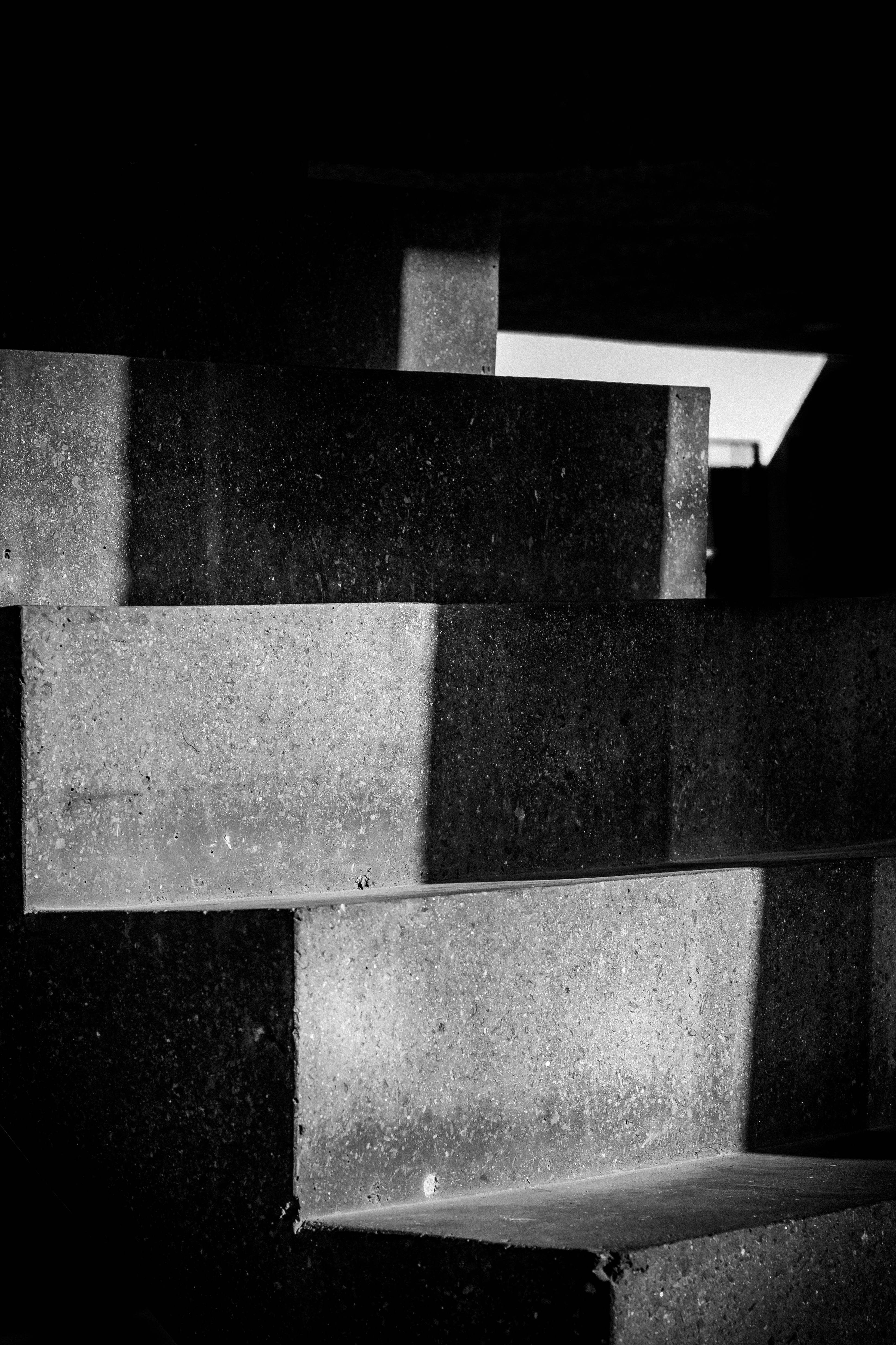 This striking black and white photograph captures the raw beauty of concrete steps, bathed in dramatic lighting that accentuates their texture and geometric precision. The composition, with its stark contrasts and minimalist aesthetic, evokes a sense of modernity and sophistication. Perfect for contemporary living spaces, this image can serve as a a focal point in a living room or as a a statement piece in an executive office, enhancing the space with its clean lines and industrial charm.