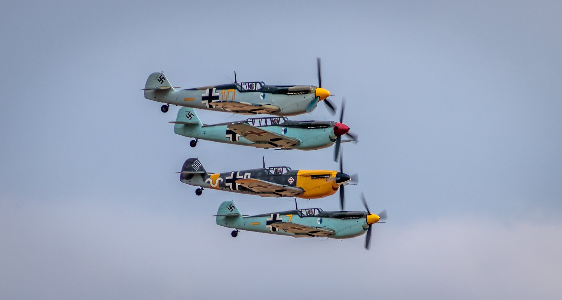 This photograph captures a breathtaking moment of four vintage fighter planes flying in perfect formation against a soft, diffused sky. The warm, golden hues of the planes' camouflage paint and the subtle interplay of light and shadow create a visually stunning composition. The image evokes a spirit of adventure and the timeless beauty of aviation history, making it a perfect focal point for any aviation enthusiast or anyone who appreciates the art of flight. Ideal for a living room, it can executive office, or a modern gallery wall, this piece is a testament to the enduring allure of aviation and the art of photography.