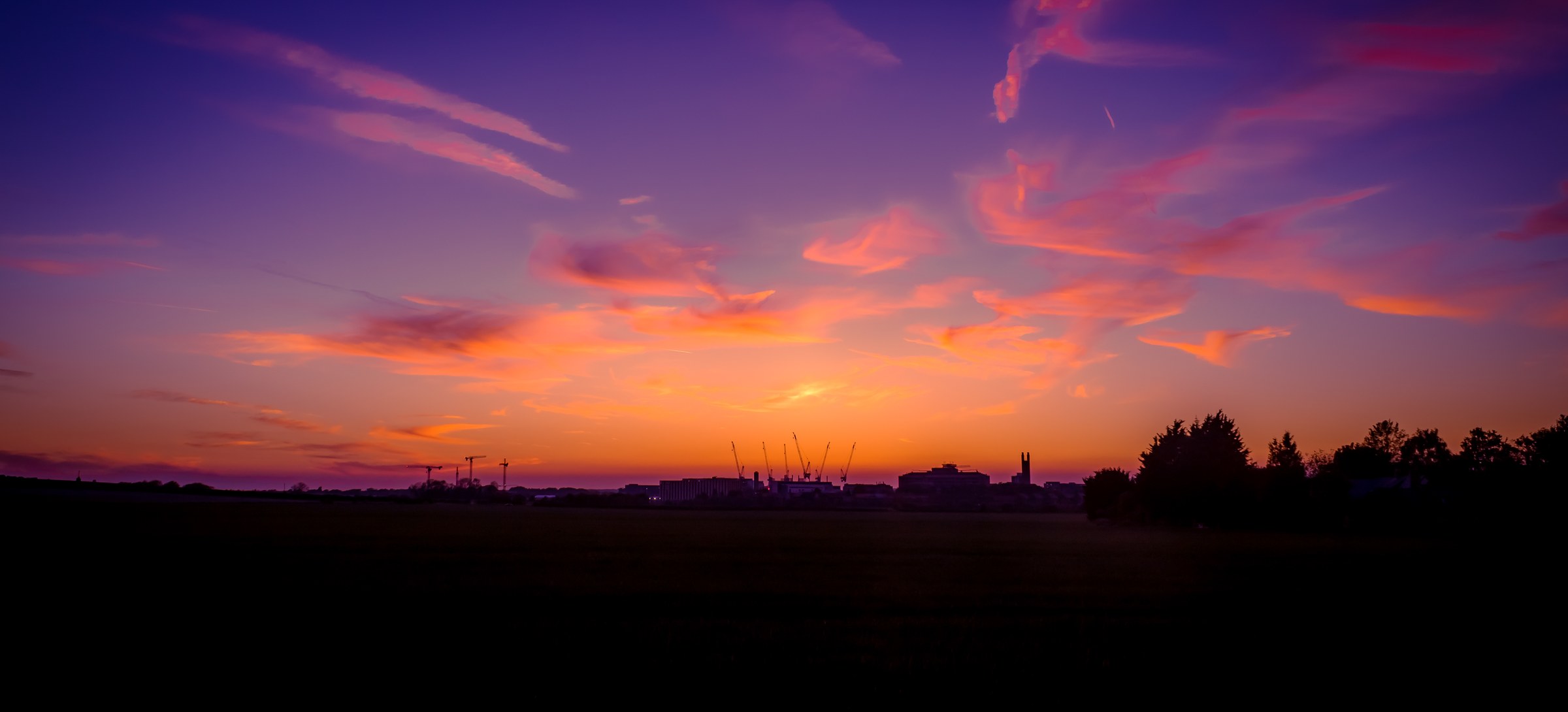 Capture the tranquil beauty of a sunset with this stunning photograph, where the sky is painted in hues of deep purple and vibrant orange, creating a mesmerizing contrast. The composition beautifully frames the horizon, with silhouettes of distant buildings and trees adding depth and context. This soft, diffused lighting enhances the ethereal quality, making it perfect for a living room as a focal piece, or for the executive office to inspire calm and creativity.