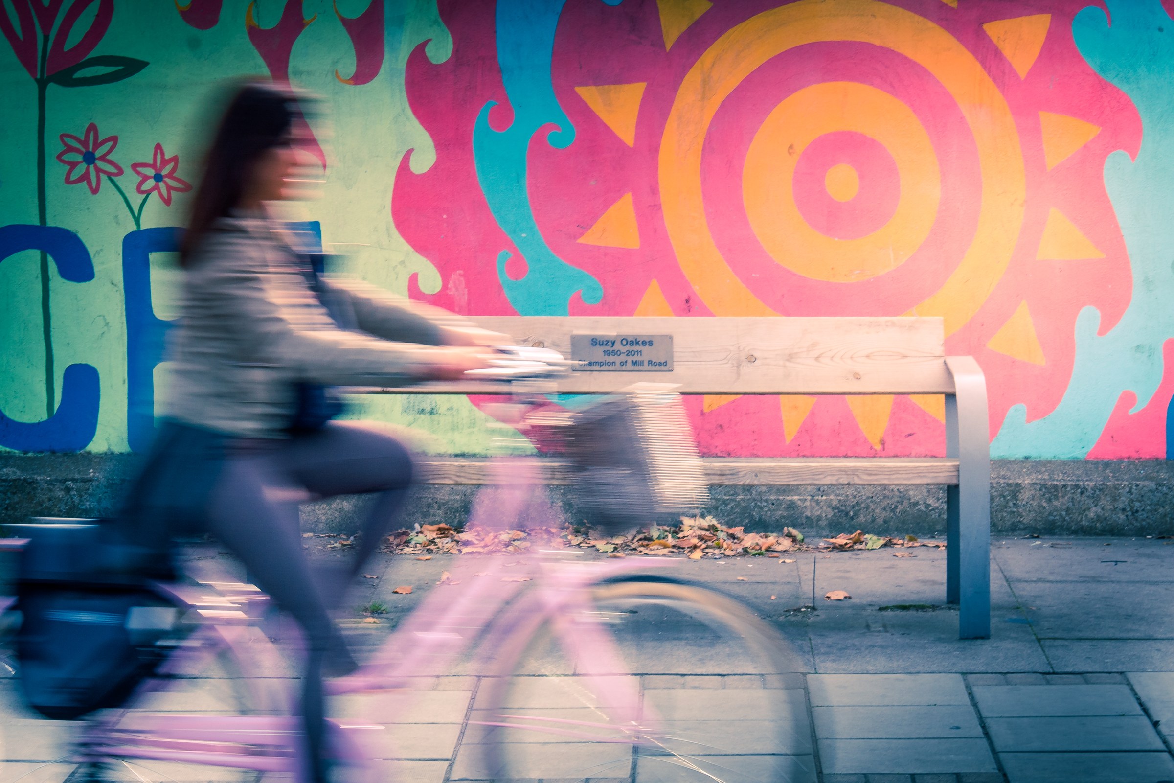 This photograph captures the essence of a serene urban journey, where a a vibrant mural backdrop contrasts beautifully with the motion blur of a cyclist. The soft, diffused lighting enhances the dreamy, nostalgic mood, making it perfect for a living room as a focal piece. The composition, with the bench and the bicycle, creates a perfect balance, making it ideal for a executive office or a modern gallery wall. The aesthetic appeal lies in its ability to evoke a feeling of freedom and creativity, making it a versatile piece for any space.