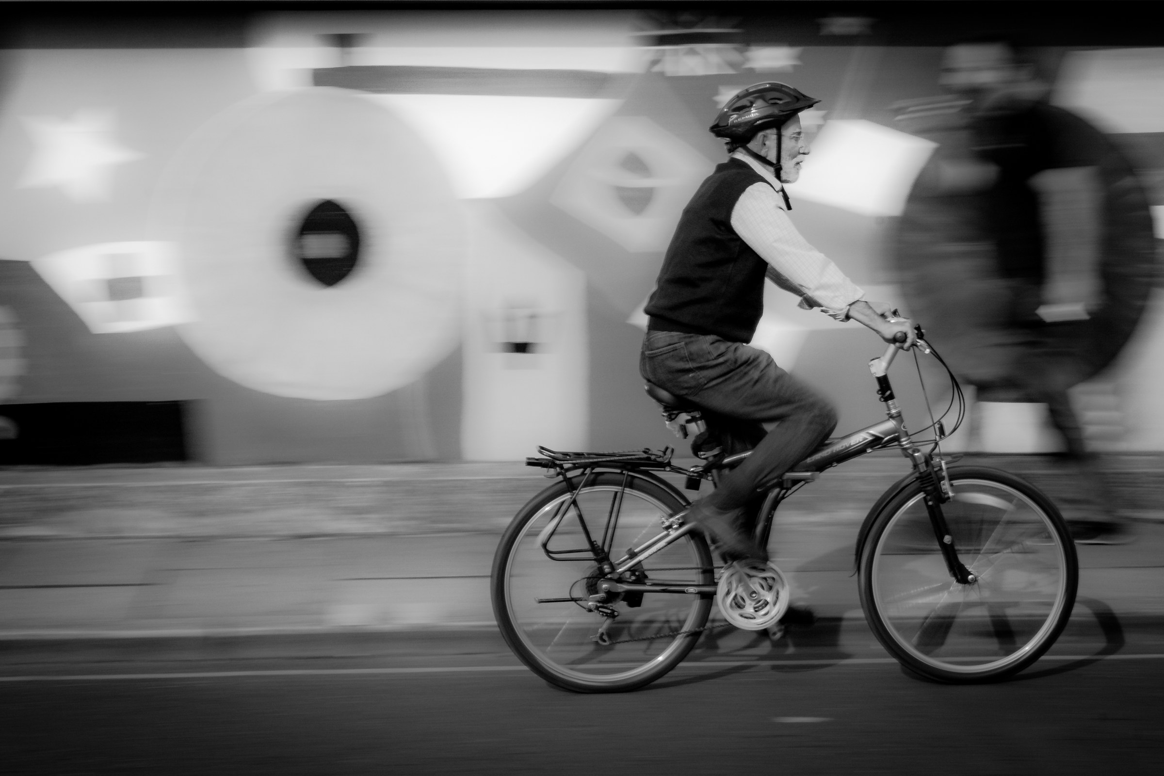 This striking black and white photograph captures the essence of urban motion and freedom. The cyclist, blurred in background, creates a dynamic sense of speed and movement, while the sharp focus on the cyclist adds a element of stillness and calm. The composition, with the cyclist positioned slightly off-center, draws the viewer's eye across the frame, enhancing the sense of journey and exploration. The high contrast and monochromatic palette lend a image a timeless quality of fine art, making it a perfect piece for a modern gallery wall or a focal point of a living room. The image evokes a feeling of adventure and the simple joy of a ride, making it a versatile addition to any space seeking to infuse a spirit of the city into its decor.