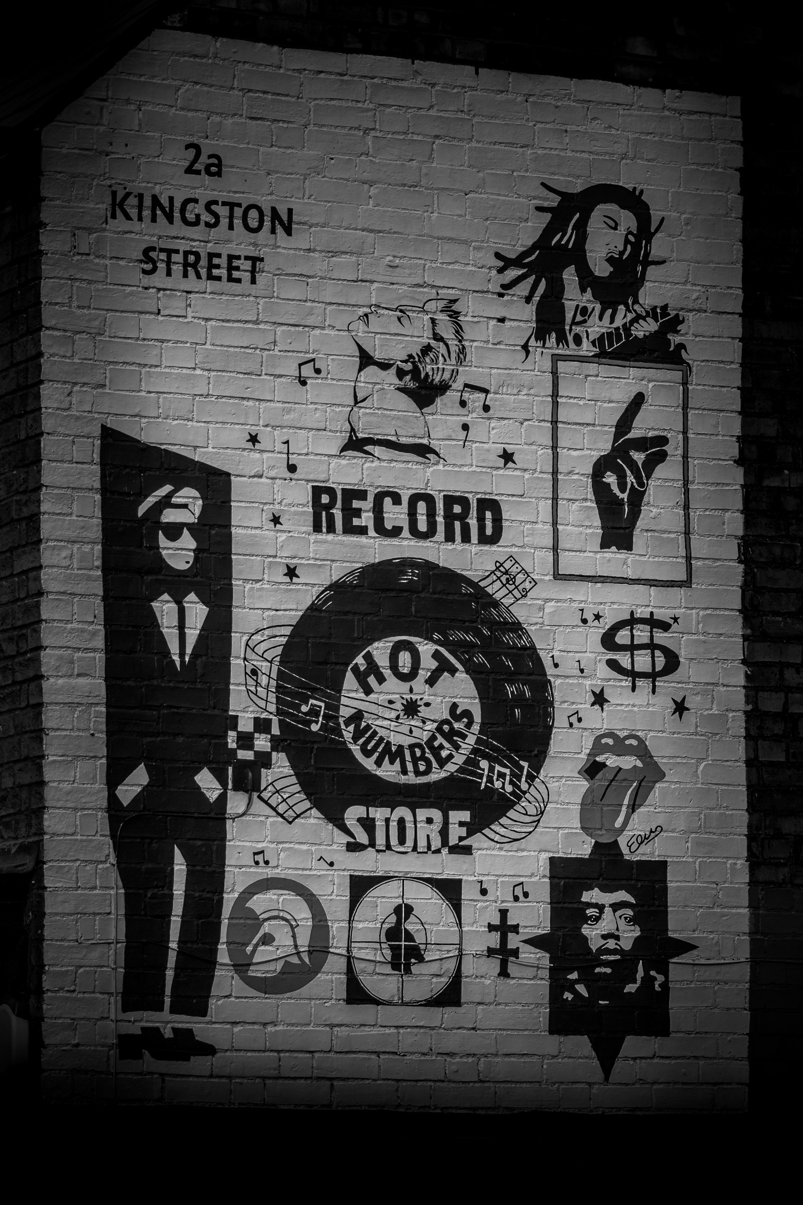 This striking black and white photograph captures the vibrant energy of Kingston Street Record Store, featuring bold, iconic symbols and a dynamic composition that evokes a sense of nostalgia and urban cool. The high-contrast lighting accentuates the textures and details of the brick wall, making it a perfect focal point for any modern art enthusiast. Ideal for a living room, it adds a perfect touch of urban sophistication and artistic flair to any space, transforming it into a a statement piece that speaks volumes about the owner's personality and taste.