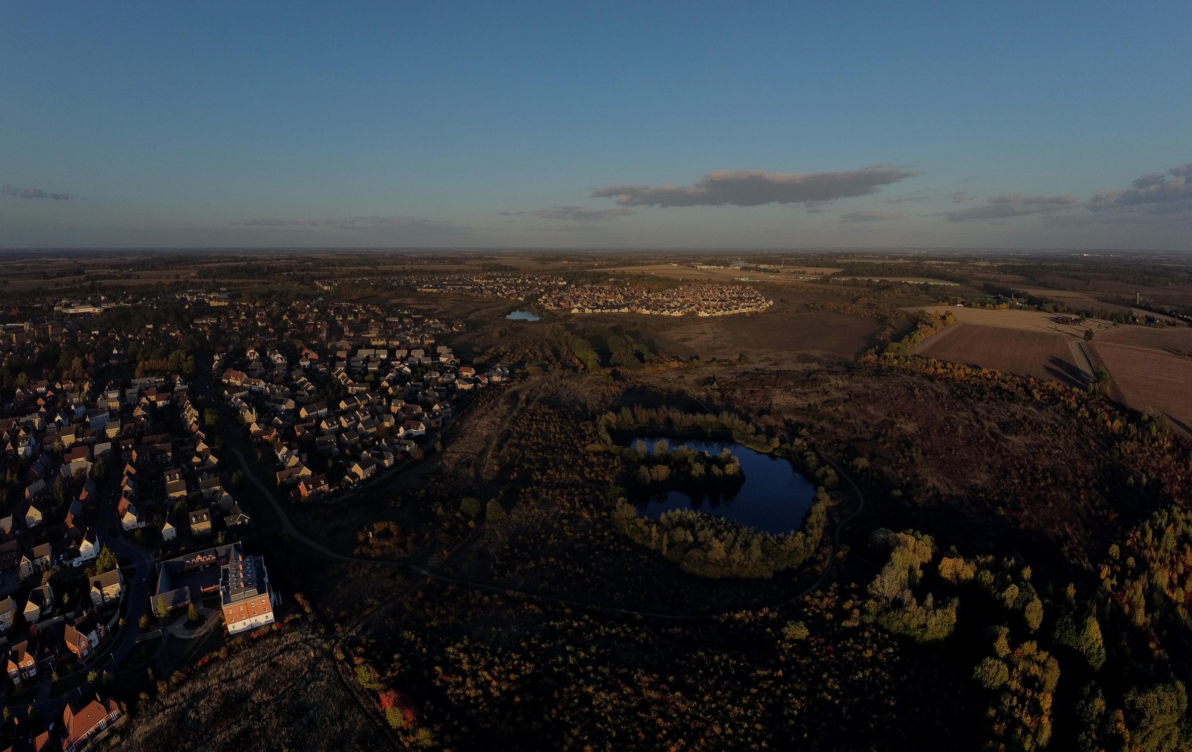 This breathtaking aerial photograph captures the tranquil beauty of a village at sunset, with the warm golden hues of the setting sun casting a perfect light over the landscape. The composition beautifully juxtaposes the dense, vibrant greenery of the forest with the serene blue of the lake, creating a perfect balance of nature and tranquility. The image evokes a feeling of peace and serenity, making it an ideal focal piece for any living room or executive office, where it can serve as a perfect backdrop to inspire calm and focus.