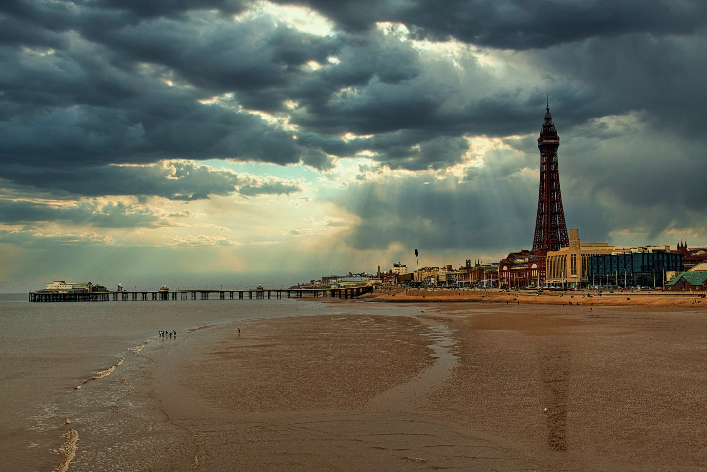 This breathtaking photograph captures the timeless beauty of Blackpool, England, with its iconic Tower and pier set against a dramatic backdrop of a North Sea. The interplay of light and shadow, with beams of sunlight piercing through the clouds, creates a perfect balance of tranquility and grandeur. The composition, with the Tower and pier leading the eye towards the horizon, offers a perfect blend of natural and architectural splendor. This rich, warm tones and the vast expanse of the beach make this image a perfect piece for any living room, creating a feeling of being right there, experiencing the serene beauty of the seaside. This image is ideal for those who appreciate the juxtaposition of nature and human-made marvels, making it a perfect focal point for any executive office or modern gallery wall.
