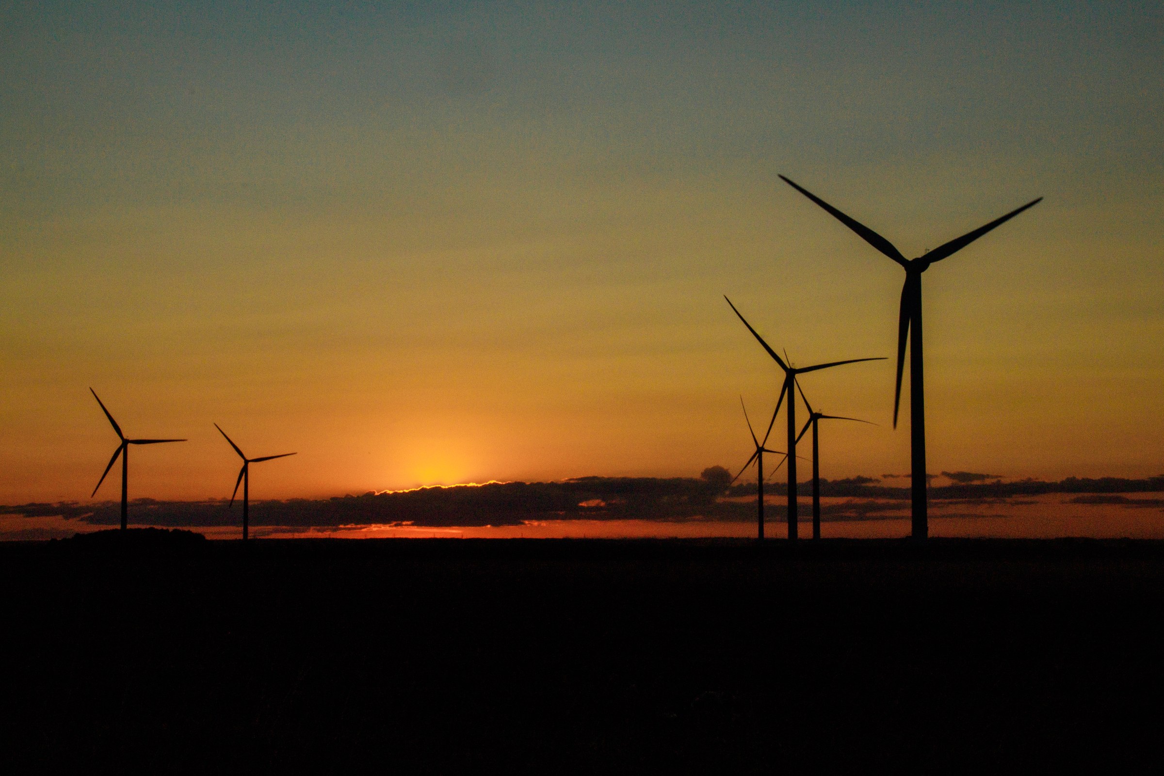 Capture the tranquil beauty of a sunset with this stunning photograph of wind turbines silhouetted against a vibrant hues of the sky. The warm, golden tones of the setting sun contrast beautifully with the dark, sleek forms of the turbines, creating a perfect balance of nature and technology. This composition, with the turbines arranged in horizon, draws the eye across the canvas, evoking a sense of peace and progress. This rich, saturated colors and the dynamic interplay of light and shadow make this image a perfect piece for any modern interior, whether as a centerpiece of a living room or as a statement wall in an executive office. Hang it in a corner of a room to subtly inspire innovation and sustainability.