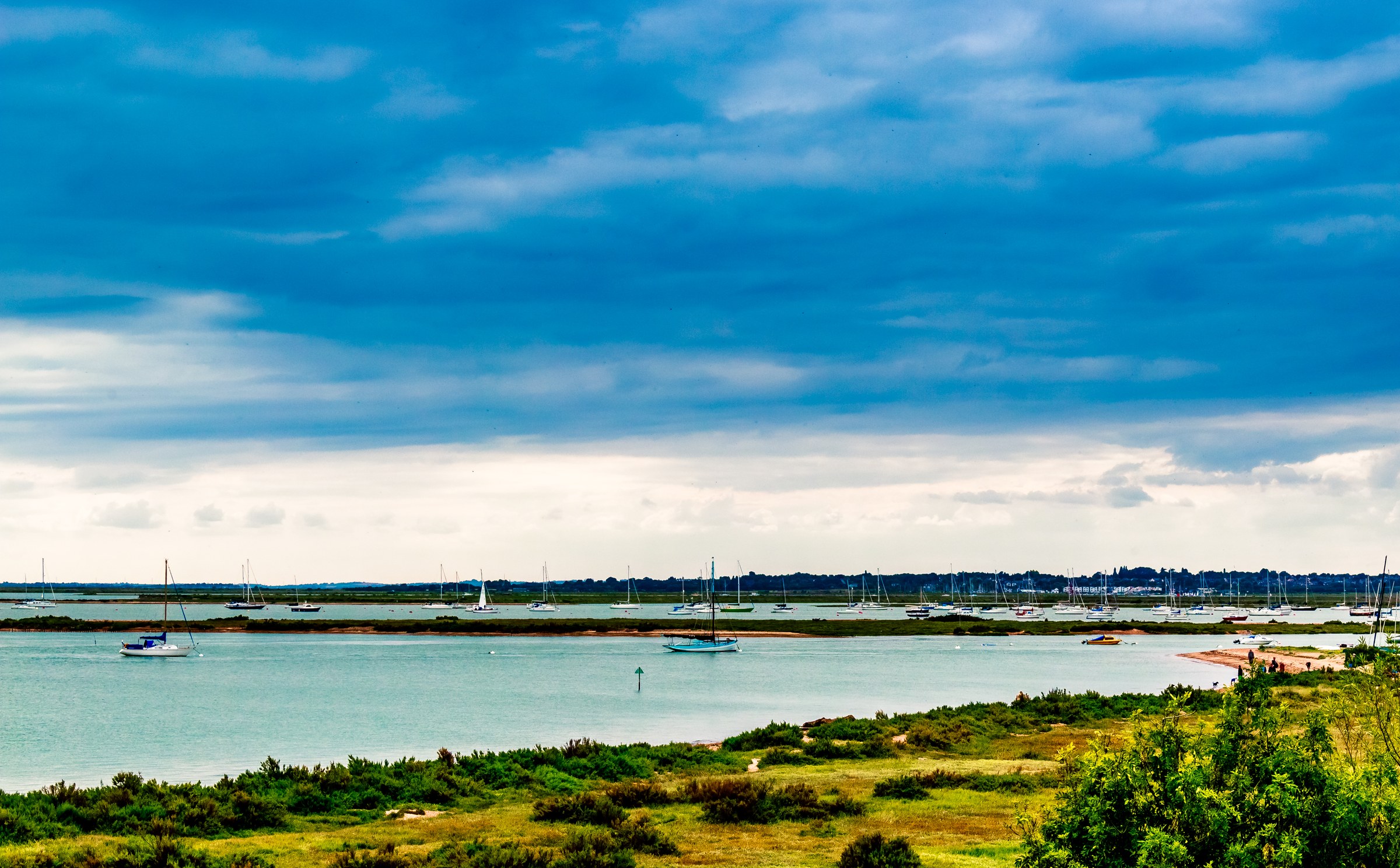 This breathtaking photograph captures the tranquil beauty of a coastal landscape under a dramatic sky, evoking a sense of peace and serenity. The vivid blues of the sky and water contrast beautifully with the lush greenery in foreground, creating a visually striking composition. The soft, diffused lighting enhances the natural colors, making this image a perfect addition to any walls of a executive office or a living room, where it can serves as a focal point, inspiring calm and contemplation.