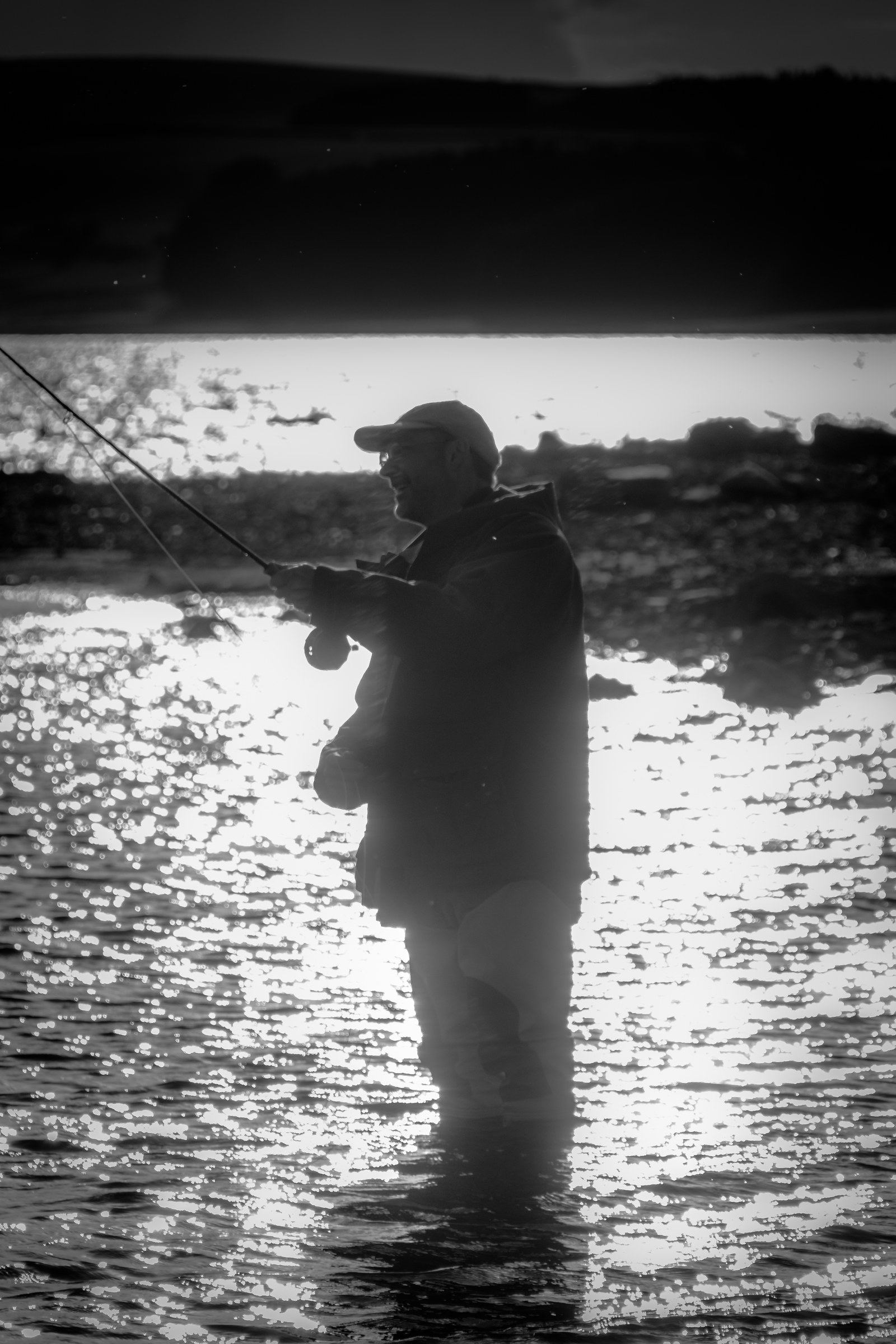 This evocative black and white photograph captures the serene essence of a lone fisherman standing in shallow water, casting his line into the tranquil expanse. The interplay of light and shadow creates a silhouette of the fisherman, emphasizing the peaceful solitude of the moment. The composition, with the fisherman positioned slightly off-center, draws the viewer's eye across the scene, inviting contemplation of the quiet beauty of nature. This image's aesthetic appeal lies in its timeless quality, making it a perfect piece for a living room focal point or an executive office where it can inspire a spirit of calm and reflection. The stark contrast and monochromatic palette lend it a perfect balance of drama and tranquility, making it a standout addition to any modern gallery wall.
