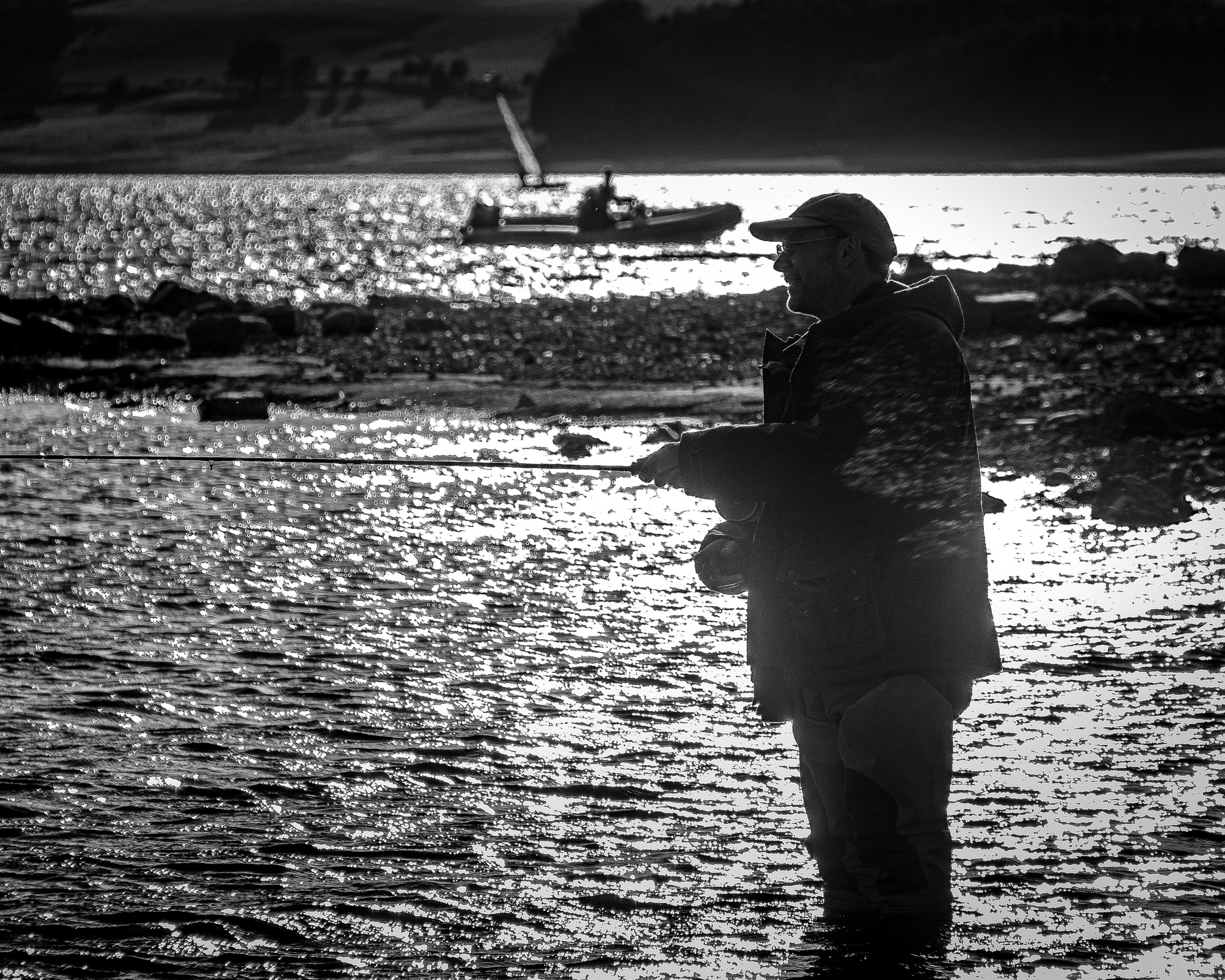 This evocative black and white photograph captures the tranquil essence of a fishing moment, where the silhouette of a fisherman stands out against the shimmering water and distant boat. The interplay of light and shadow creates a dramatic and contemplative mood, inviting viewers to reflect on solitude and the simple pleasures of nature. The composition, with the fisherman positioned centrally, draws the eye across the scene, from the foreground to the background, enhancing the sense of depth and space. This aesthetic appeal lies in its timeless quality, making it a perfect piece for a living room focal point or an executive office where it can inspire a spirit of calm and introspection.