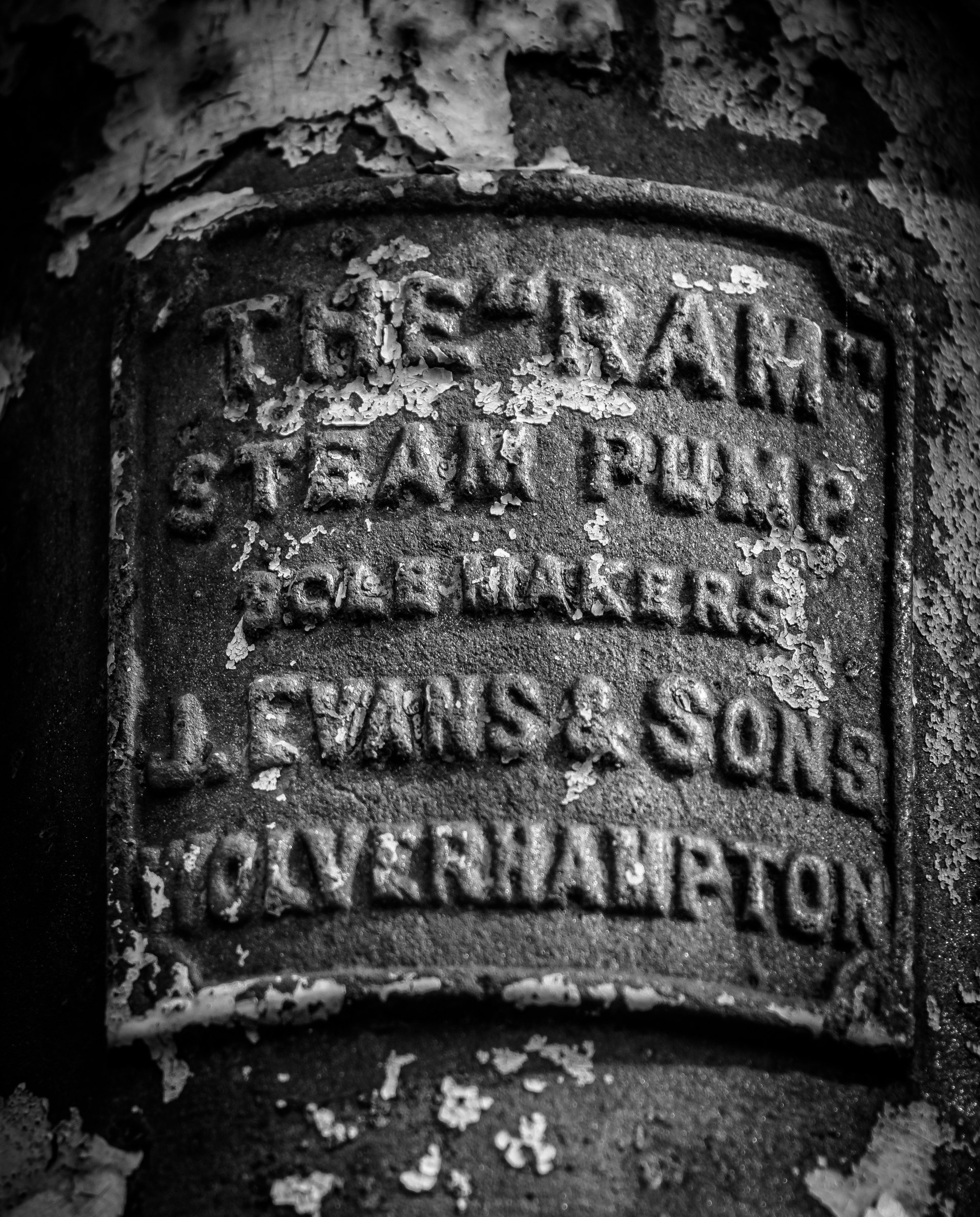 This evocative black and white photograph captures the rugged charm of a vintage steam pump plaque, engraved with the name 'The Fram Steam Pump' and 'J. Evans & Sons, Wolverhampton.' The weathered texture and peeling paint evoke a sense of history and industrial heritage, making it a perfect piece for those who appreciate the beauty of the past. The dramatic lighting accentuates the plaque's details, creating a perfect focal point for a living room or a modern gallery wall. Its aesthetic appeal lies in its ability to blend seamlessly with contemporary decor while adding a touch of industrial nostalgia.