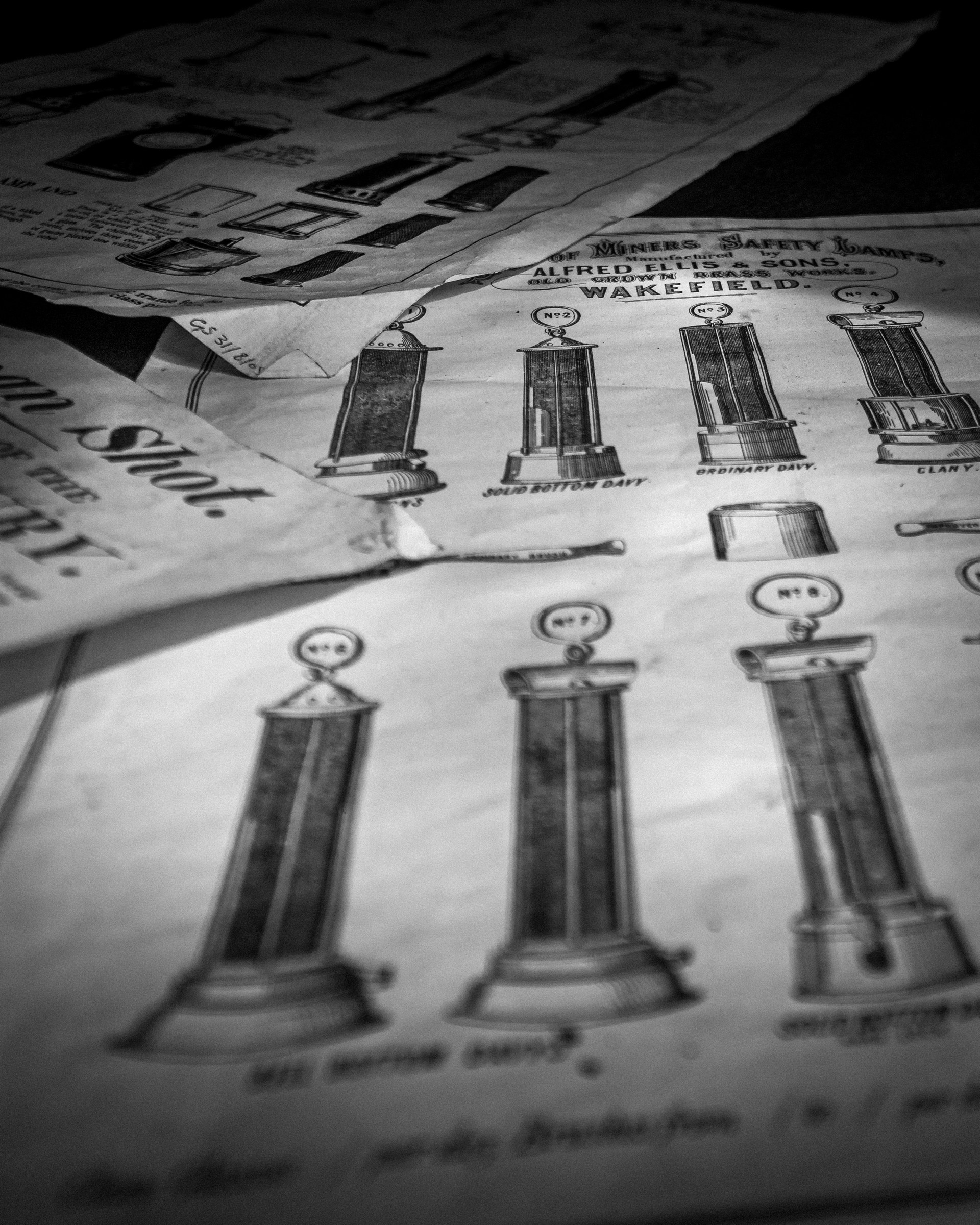 This striking black-and-white photograph captures the essence of industrial design, featuring a intricate details of vintage safety lamps from Alfred Ellis & Sons, Wakefield. The soft, diffused lighting enhances the texture and depth of the image, creating a moody and nostalgic atmosphere. The composition, with its focus on the lamps, draws the viewer's eye, making it a perfect focal point for any living room or executive office. Its aesthetic appeal lies in its ability to blend seamlessly with modern decor, adding a perfect touch of industrial chic to any space.