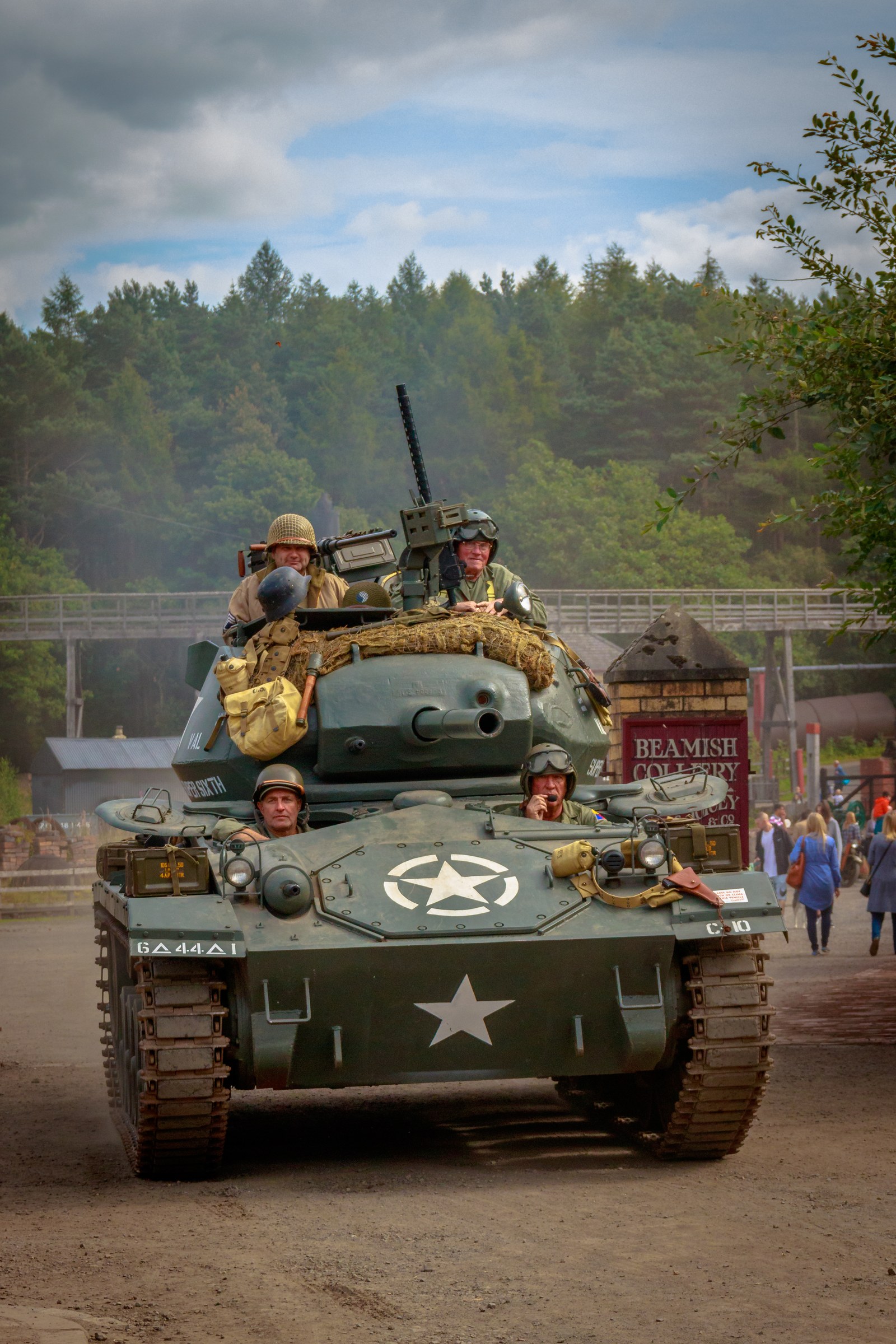 This photograph captures the timeless allure of a past, featuring a vintage tank adorned with soldiers in period attire, set against a serene backdrop of a countryside. The warm, natural light enhances the rich greens of the forest and the rugged texture of the tank, creating a perfect balance of nostalgia and adventure. The composition, with the tank as the central focus, draws the viewer into a scene, evoking a spirit of camaraderie and historical significance. This image is ideal for wall decor in executive office, where it can serve as a powerful reminder of resilience and the human spirit in the face of adversity.