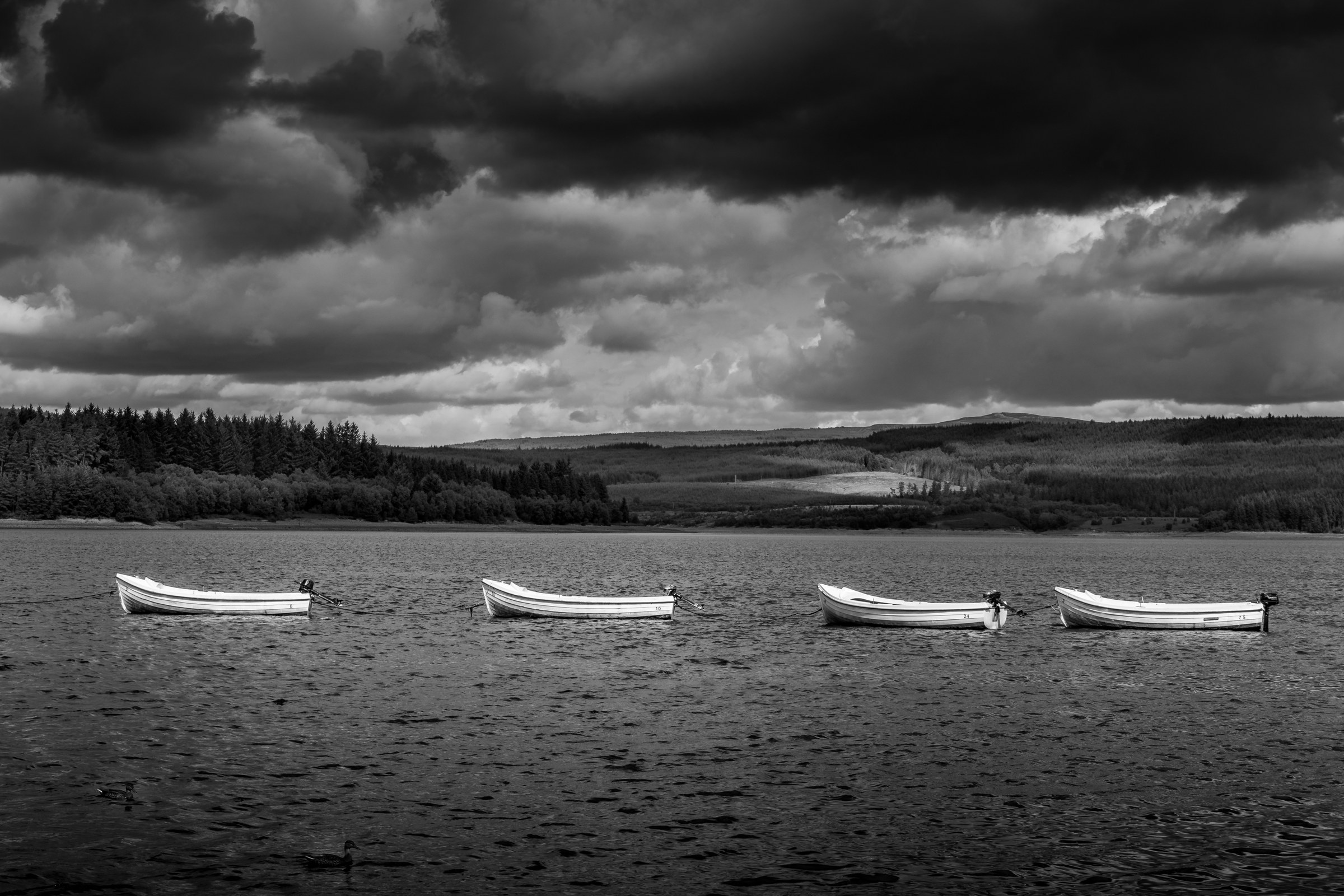 Four small rowing boats moored on a calm lake under a dramatic sky, creating a serene and contemplative scene.