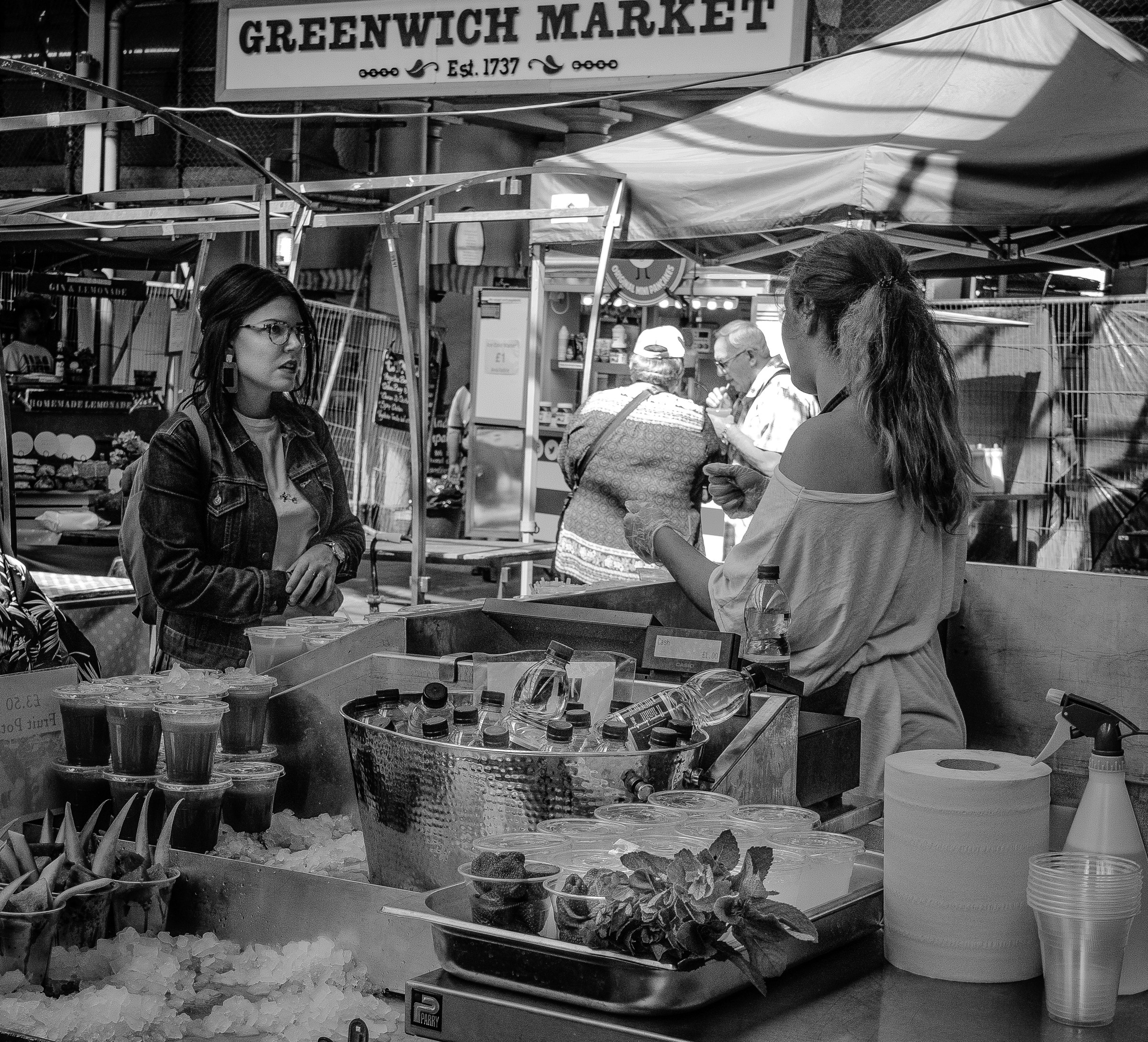 This evocative black and white photograph captures the lively essence of a Greenwich Market, with its bustling atmosphere and vibrant street life. The high contrast and monochromatic palette enhance the textures and details of the market scene, creating a perfect mood for a modern, sophisticated space. The composition, with its dynamic interplay of light and shadow, draws the viewer into the heart of the market, making it a ideal focal point for a living room or a executive office. The aesthetic appeal lies in its timeless quality, making it a perfect addition to a modern gallery wall, where it can inspire and captivate onlookers with its raw, authentic urban charm.