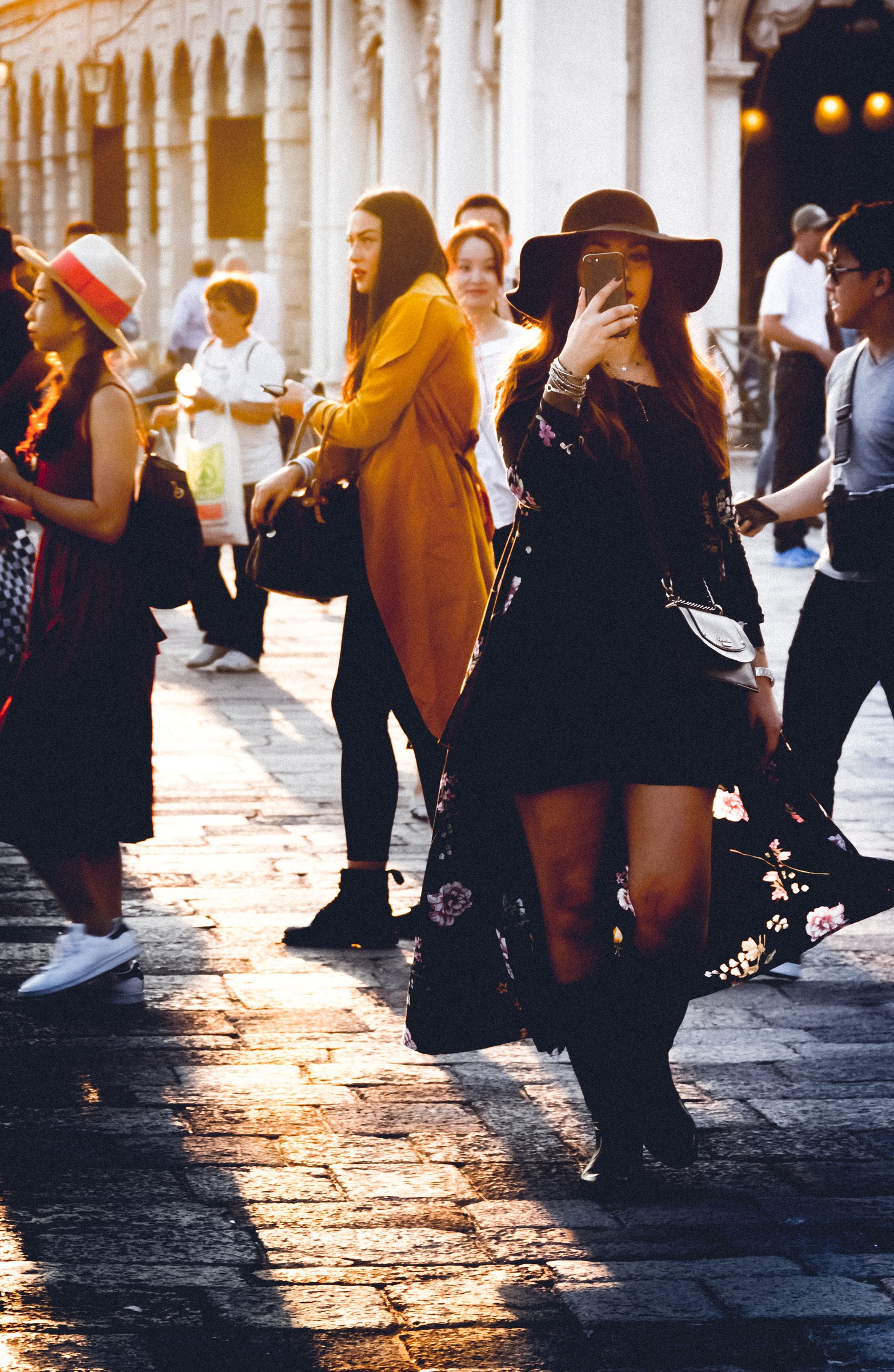 This photograph captures a essence of urban life, where the interplay of light and shadow creates a serene yet vibrant atmosphere. The golden hour sunlight bathes the scene in, casting long shadows and highlighting the textures of the cobblestone street and the rich colors of the subjects' attire. The composition, with its dynamic movement and candid moments, invites viewers to pause and reflect on the beauty of everyday life. Perfect for a living room as a focal piece, it adds a perfect touch of modern elegance and artistic flair to any space.