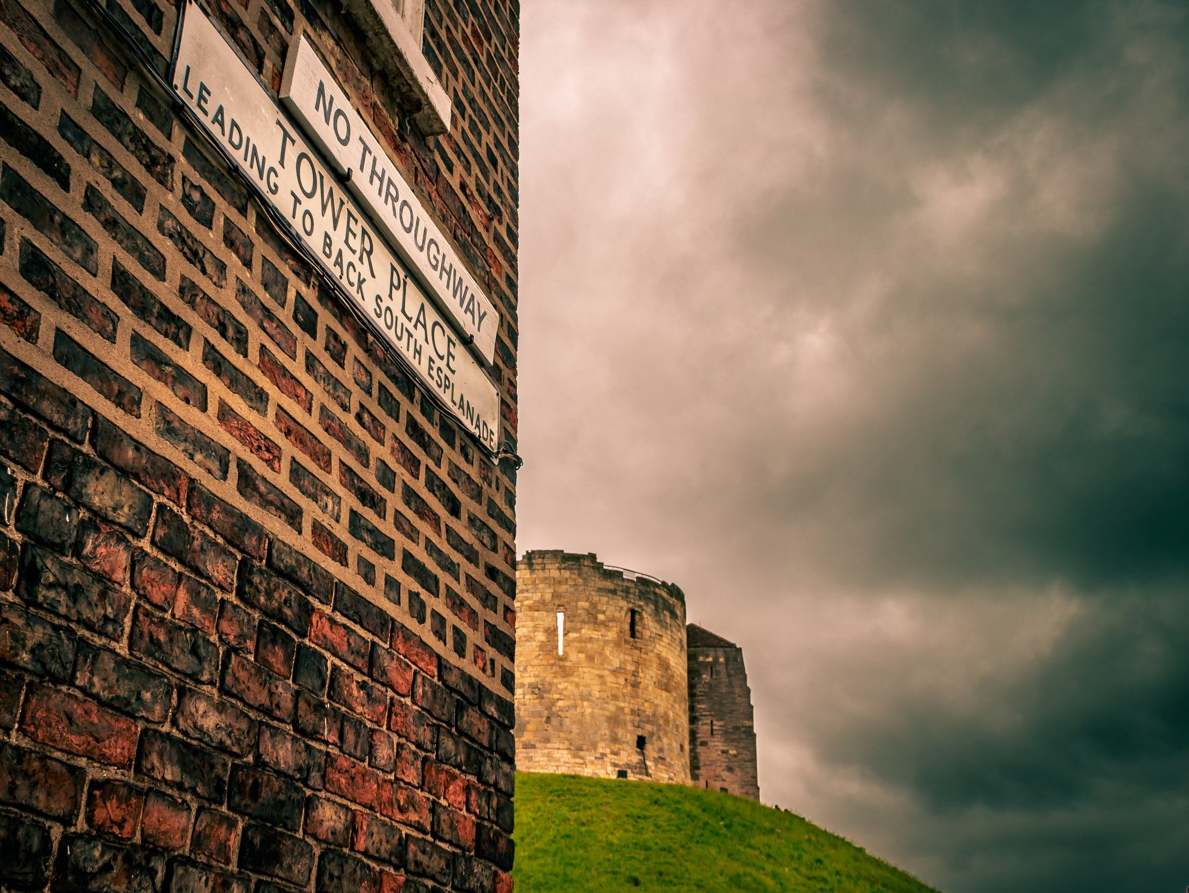 This fine-art print captures the haunting beauty of a medieval castle under a stormy sky, evoking a mood of mystery and history. The dramatic lighting and composition highlight the textures of the brick wall and the castle's stone structure, creating a perfect piece for a modern gallery wall or a executive office. The dark, moody tones make it a ideal focal point for any living room, adding a perfect touch of sophistication and intrigue to any space.